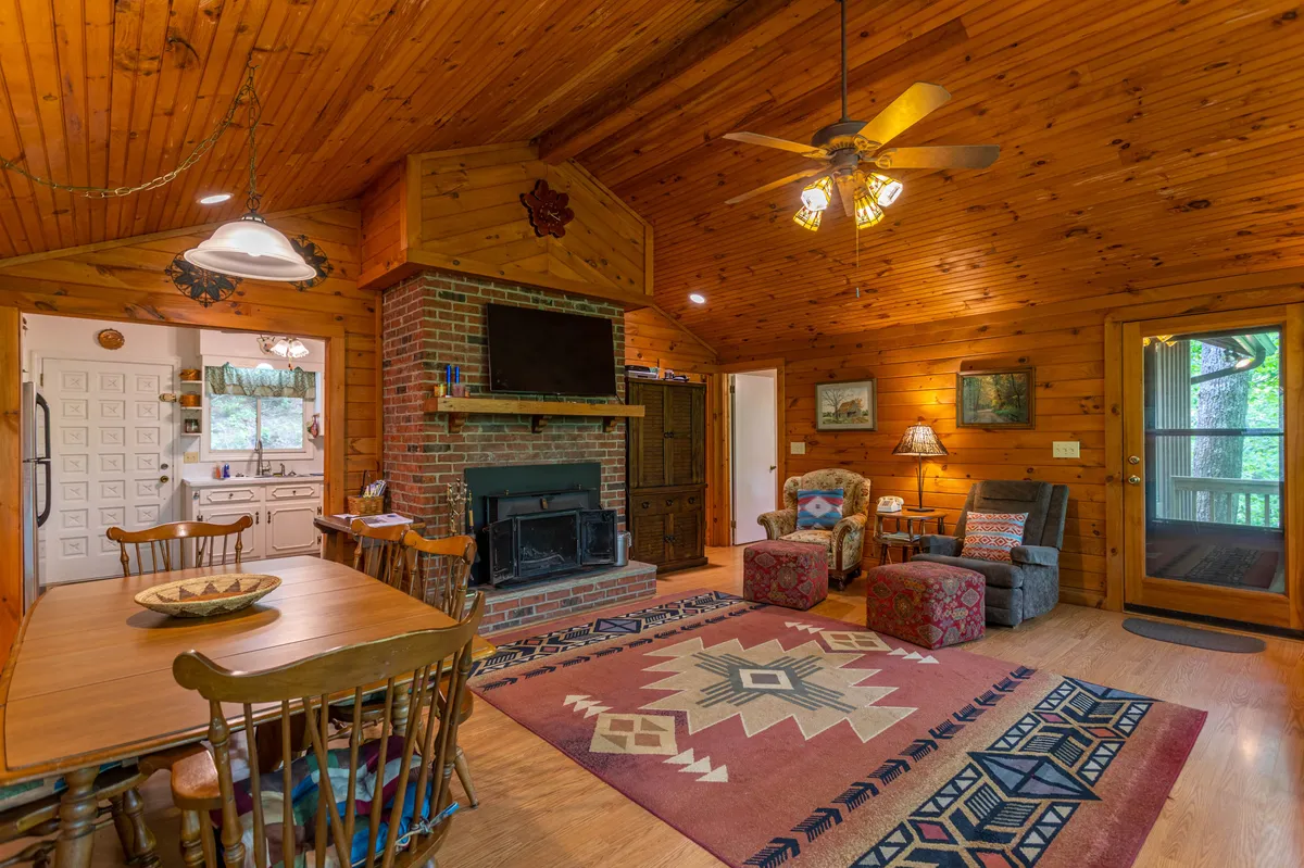 A cozy interior space featuring a stone fireplace, dining table, area rug, and comfortable armchairs. A TV is visible, providing entertainment options like satellite TV and a DVD player. The setting is designed for family relaxation, movie nights, and festive gatherings.