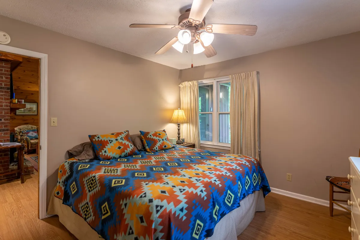 A cozy bedroom with a colorful patterned bedspread, a window adorned with curtains allowing natural light to filter in, and a bedside table with a lamp. The arrangement invites relaxation, with a sense of warmth and comfort perfect for unwinding after a day outdoors.
