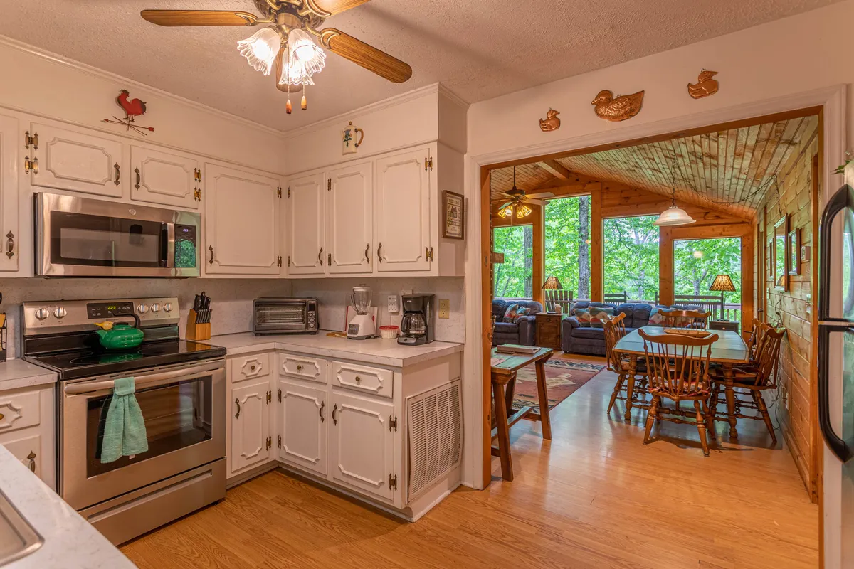 The image displays a bright and welcoming kitchen area featuring stainless steel appliances, white cabinetry, green cookware, and an open doorway leading to a dining space. The design suggests easy movement between cooking and dining, reinforcing the kitchen’s central role in family activities.