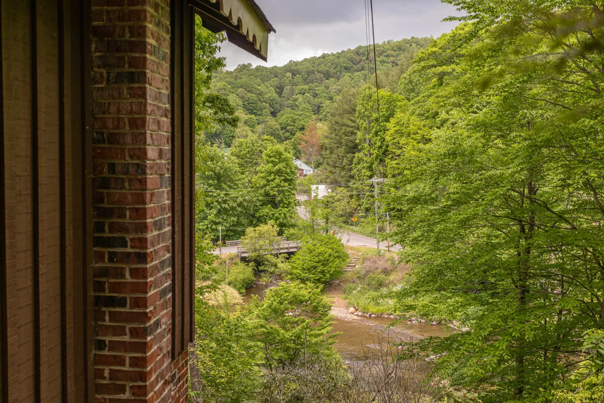 A wide view of the river winds through lush greenery, with distant buildings adding a sense of place and community. The calm water invites gentle outdoor activities like kayaking or riverside strolls.